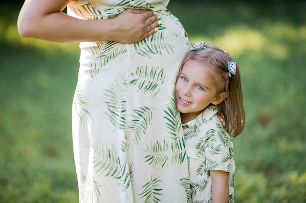 Una bella giovane mamma incinta e la sua piccola figlia stanno raccogliendo fiori in un campo. Maternità. Una famiglia. Estate.