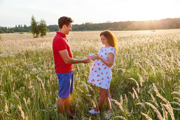 Una bella immagine all'aperto di un giovane che fa un regalo a sua moglie incinta. Servizio fotografico di famiglia incinta in natura