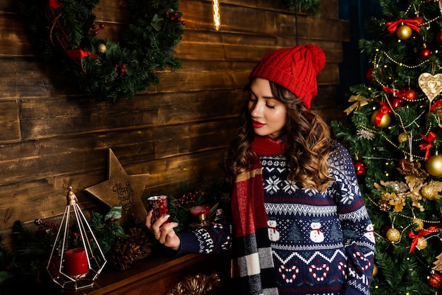 Una bella mora sta accanto al caminetto sullo sfondo di un albero di Natale e decorazioni natalizie