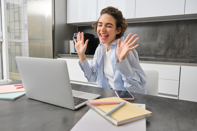 Una bella ragazza agita le mani alla telecamera del portatile dice ciao ai colleghi di lavoro si collega a una riunione di lavoro online