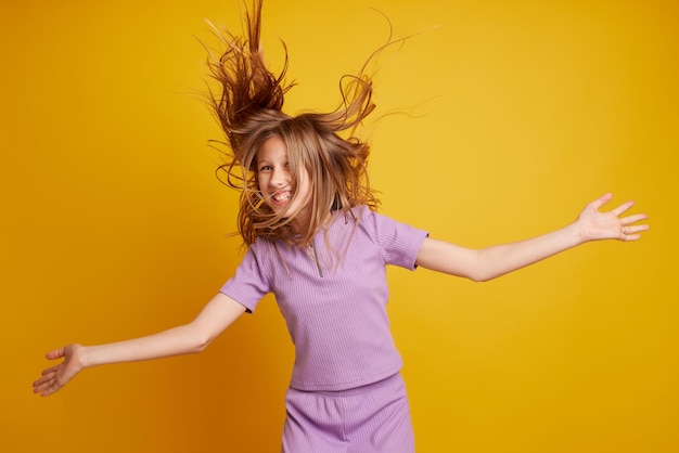 Una bella ragazza balla ridendo e divertendosi su uno sfondo giallo pulito