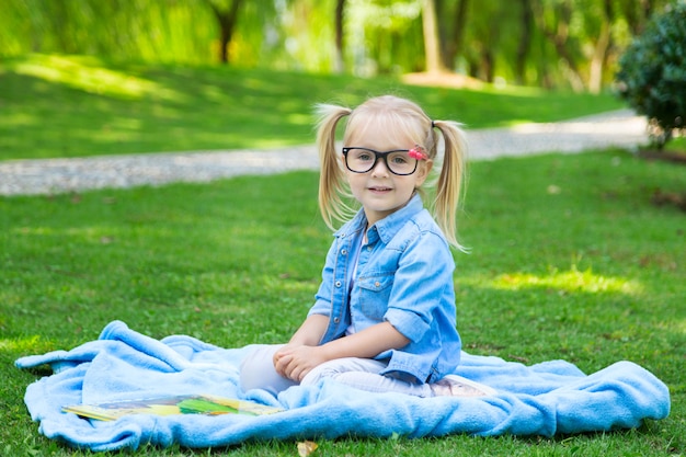 Una bella ragazza bionda con i capelli biondi e occhiali da lettura leggendo un libro su un parco