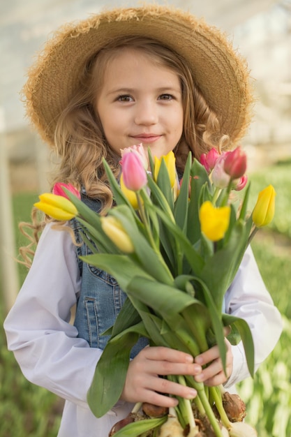 una bella ragazza bionda con un cappello di paglia tiene in mano tulipani primaverili gialli e rosa