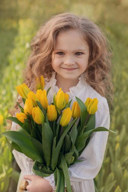 una bella ragazza bionda dai capelli lunghi con una camicetta bianca tiene in mano un mazzo di tulipani gialli