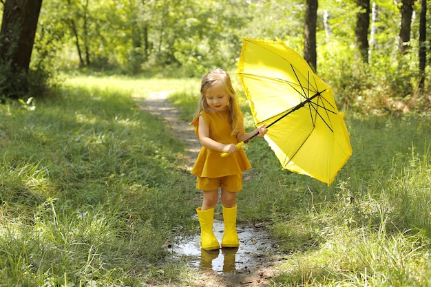 una bella ragazza bionda in un abito di lino con stivali gialli con un ombrello giallo nel parco