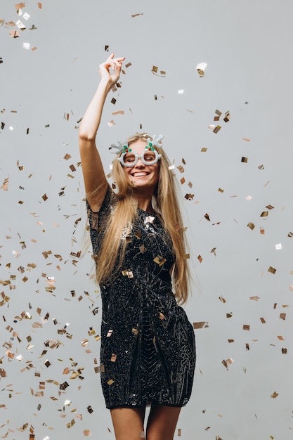 Una bella ragazza bionda sta ballando sotto coriandoli scintillanti Concetto di festa di Capodanno