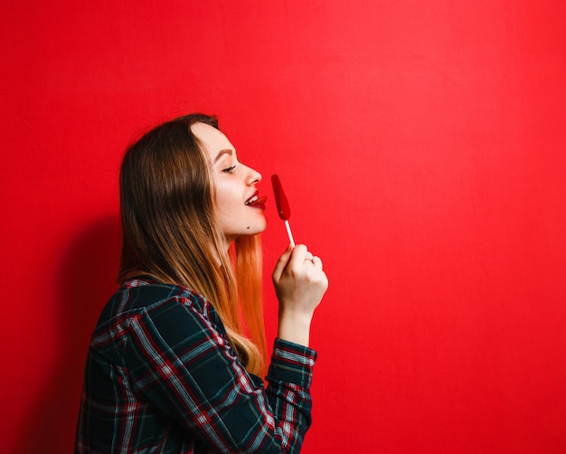 Una bella ragazza bruna con una caramella in mano divertirsi su uno sfondo rosso.