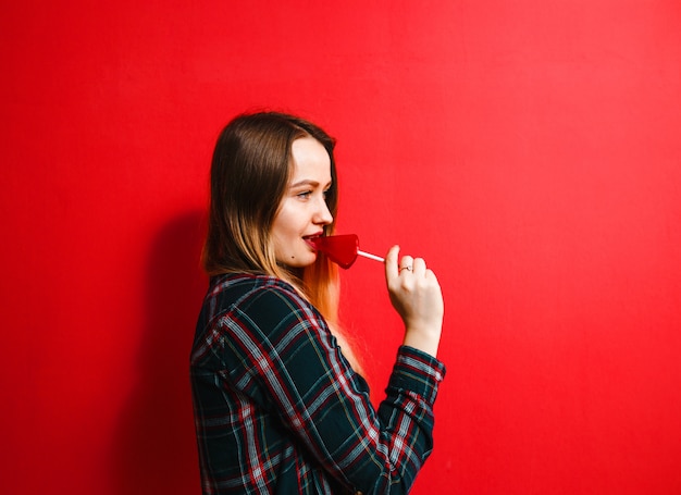 Una bella ragazza bruna con una caramella in mano divertirsi su uno sfondo rosso.