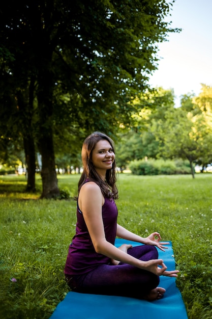 Una bella ragazza bruna è seduta su una stuoia di yoga blu in una posa Namaste e sorridente