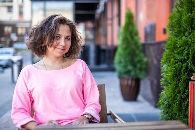 Una bella ragazza bruna in abiti alla moda è seduta in un caffè estivo.