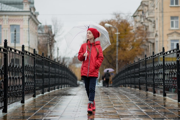 Una bella ragazza cammina sul ponte sotto la pioggia con un ombrello trasparente. Autunno.