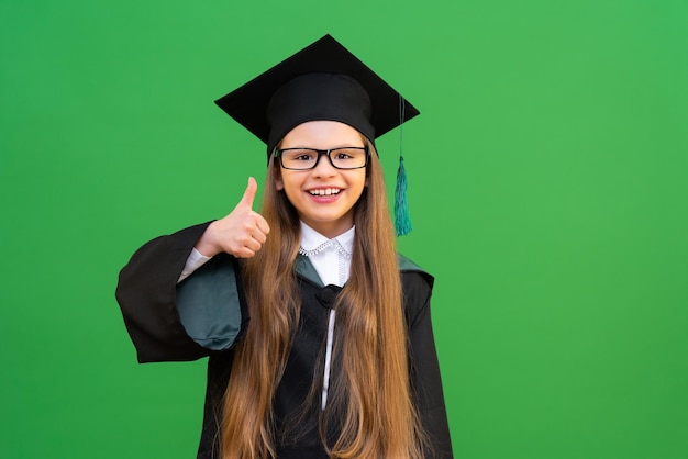 Una bella ragazza carina in uniforme scolastica molto felice di ricevere un'istruzione agli esami scolastici alla fine dell'anno scolastico una studentessa in un abito da maestro e cappello una ragazza su uno sfondo verde isolato