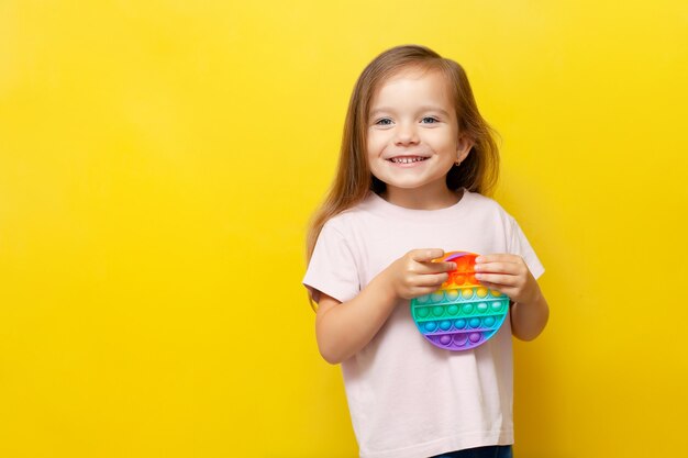 Una bella ragazza carina tiene in mano un giocattolo pop it colorato e sorride Sfondo giallo