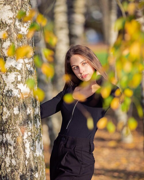 Una bella ragazza che posa vicino a un abete in un parco d'autunno