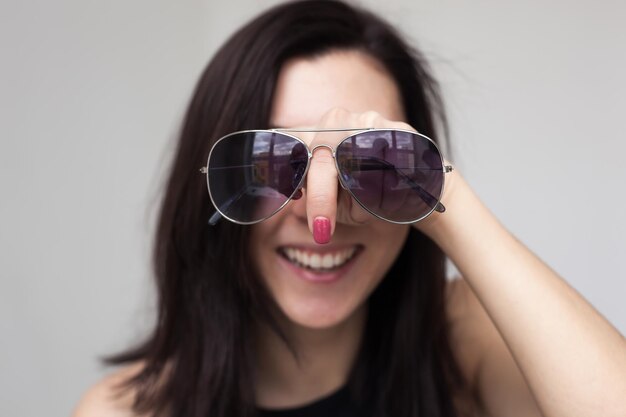 Una bella ragazza che prova gli occhiali da sole Si sta divertendo e scherzando Puntando il dito come un naso enorme