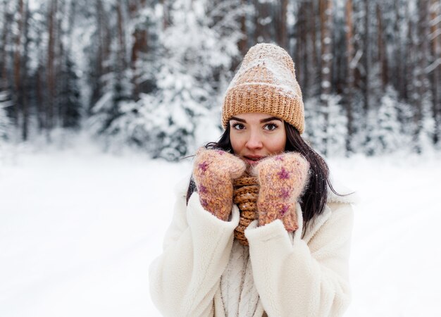 Una bella ragazza che ride felice in guanti e una sciarpa-cappello invernale, ricoperta di fiocchi di neve.