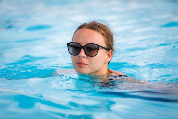 Una bella ragazza con gli occhiali da sole nuota in piscina