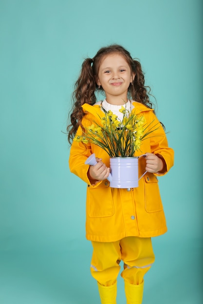 una bella ragazza con i capelli ricci in una giacca gialla tiene un annaffiatoio con fiori
