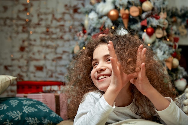 Una bella ragazza con i capelli ricci scuri si trova nel soggiorno vicino al camino Concetto di Capodanno Emozioni divertenti nella giornata invernale