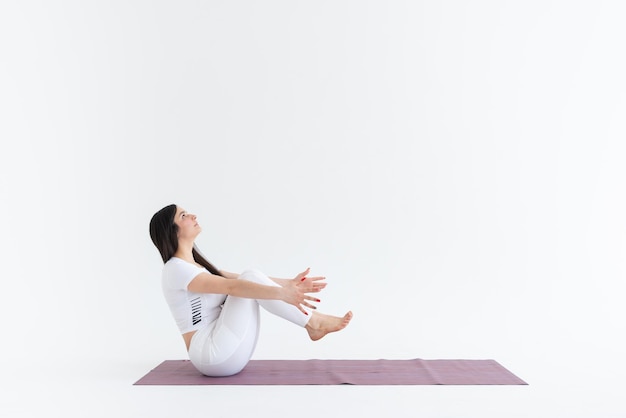 Una bella ragazza con i capelli scuri si trova nella posa di Paripurna Navasana su uno sfondo bianco