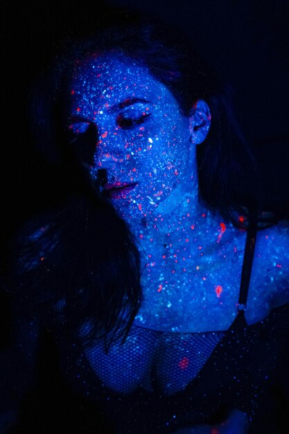 Una bella ragazza con il trucco di vernici ultraviolette fuma Rilascia fumo dalla bocca Vacanze di colori agrifoglio Libro da colorare festivo colorato luminoso Trucco fluorescente sul viso