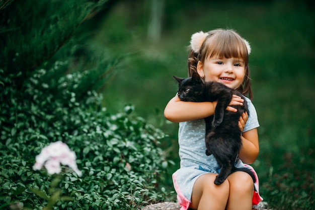 Una bella ragazza con le code di cavallo tiene in braccio un gattino nero. Intrattenimento all'aperto e concetto di passatempo.