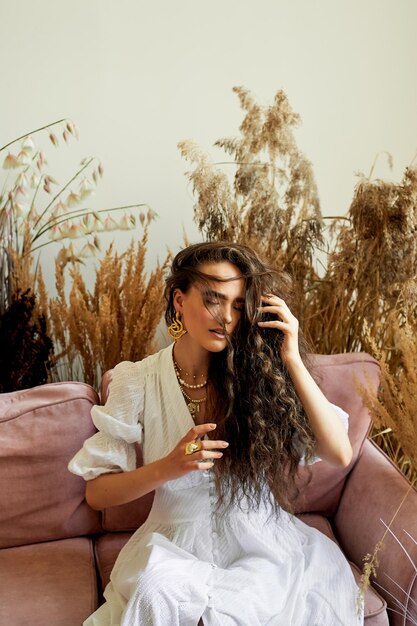 Una bella ragazza con lunghi capelli ricci in un abito lungo bianco si muove in modo dinamico Studio fotografico con cereali Moda e bellezza