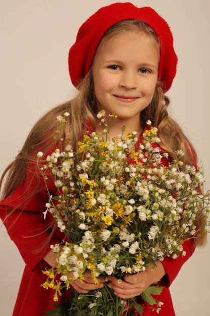 una bella ragazza con un cappotto rosso e un berretto rosso tiene in mano fiori di campo