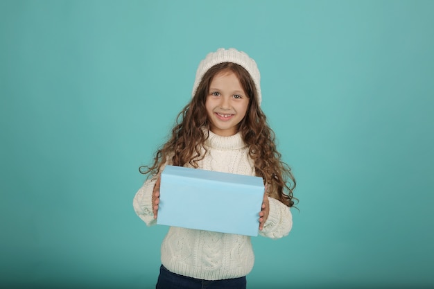 una bella ragazza con un maglione bianco e un cappello invernale bianco tiene una confezione regalo