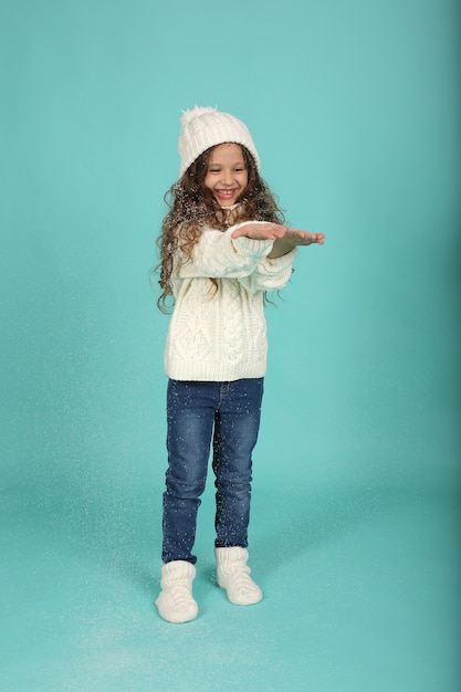 una bella ragazza con un maglione bianco un cappello invernale bianco calzini e jeans bianchi sta soffiando la neve