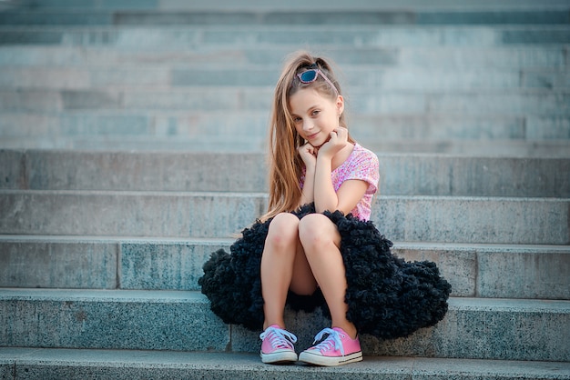 Una bella ragazza con un soffice tutu nero gonna e scarpe da ginnastica rosa si siede sui gradini.