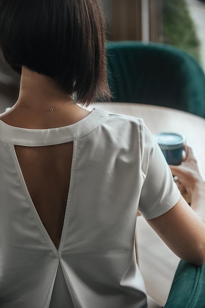 una bella ragazza con un vestito bianco con la schiena aperta si siede a un tavolo in un caffè con una tazza di tè