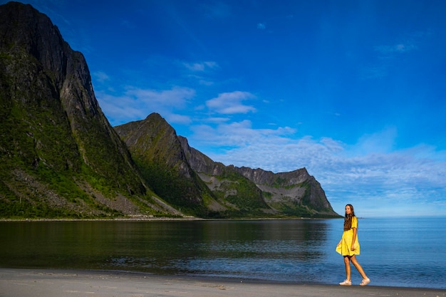 una bella ragazza con un vestito giallo cammina su una spiaggia circondata da possenti montagne, senja, norvegia