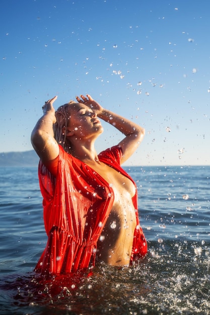 Una bella ragazza con un vestito rosso sulla spiaggia all'ora d'oro