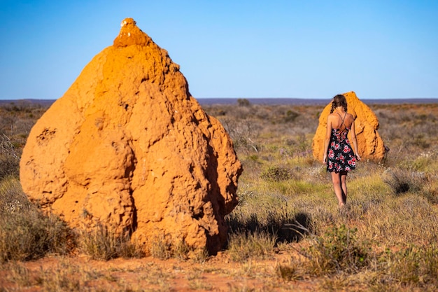 Una bella ragazza con un vestito si trova vicino a un enorme termitaio nel deserto dell'Australia occidentale