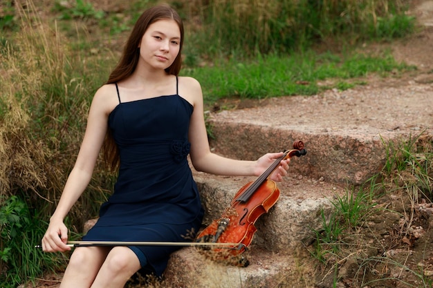 Una bella ragazza con un violino si siede sui gradini della natura