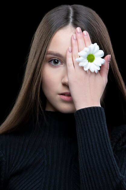 Una bella ragazza con una bellezza naturale tiene un fiore bianco vicino al suo occhio