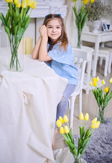 Una bella ragazza con una camicia blu si siede sullo sfondo di bouquets con tulipani gialli