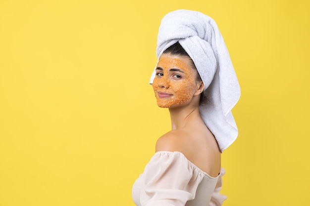 Una bella ragazza con una maschera di scrub sul viso posa per la telecamera e sorride contro un giallo