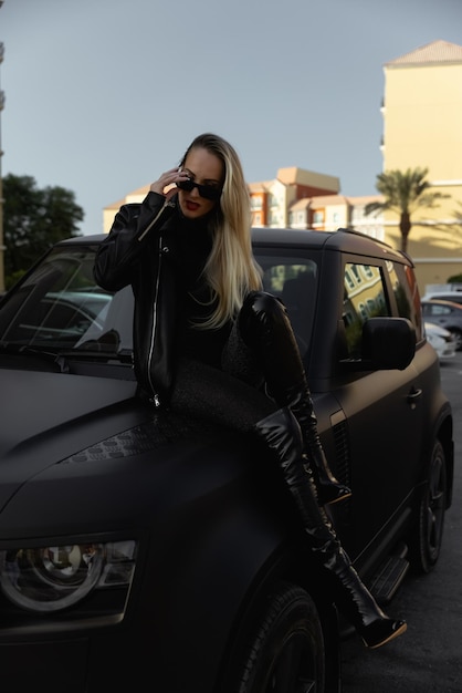 Una bella ragazza dai capelli biondi con una grande macchina nera in un vestito con la schiena scoperta. Capelli lunghi e