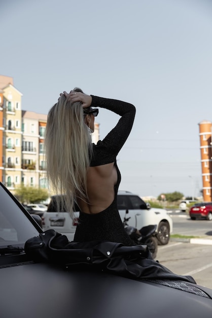 Una bella ragazza dai capelli biondi con una grande macchina nera in un vestito con la schiena scoperta. Capelli lunghi e