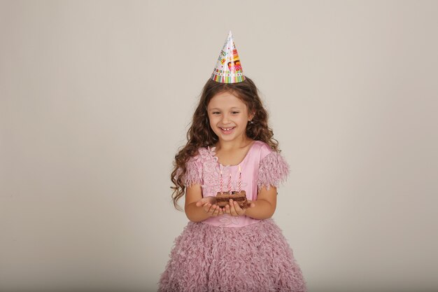 una bella ragazza dai capelli castani con i capelli ricci in un vestito rosa tiene un pezzo di torta di compleanno