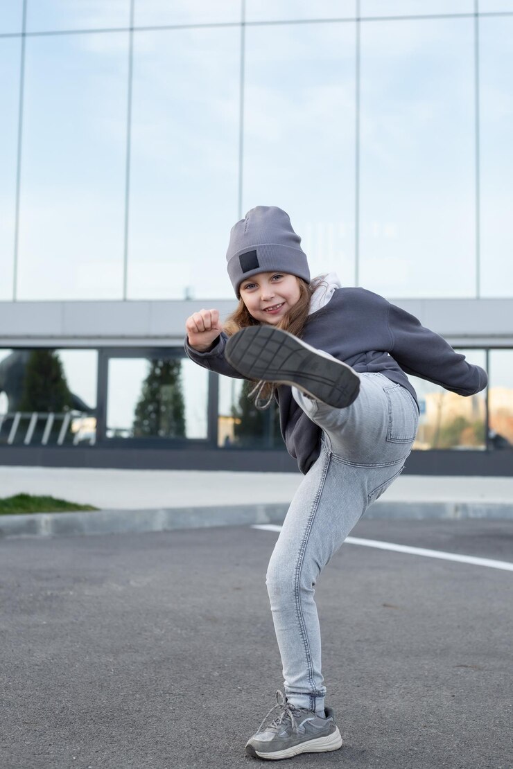 una bella ragazza di 6 anni in jeans, felpa con cappuccio e cappello grigio fa un calcio nel telaio sorride