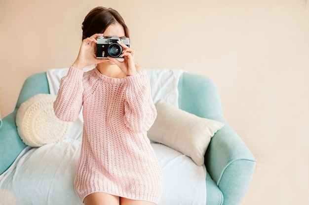 Una bella ragazza di aspetto europeo tiene in mano una macchina fotografica d'epoca in una casa accogliente