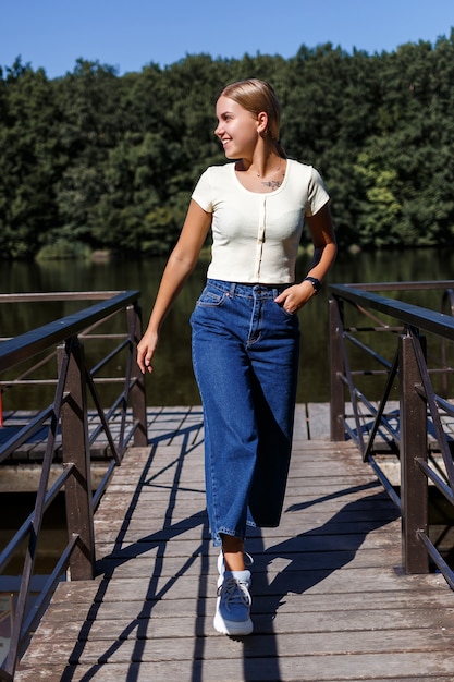 Una bella ragazza di aspetto europeo. Una giovane donna sta camminando lungo il fiume. Vestito con jeans e maglietta.