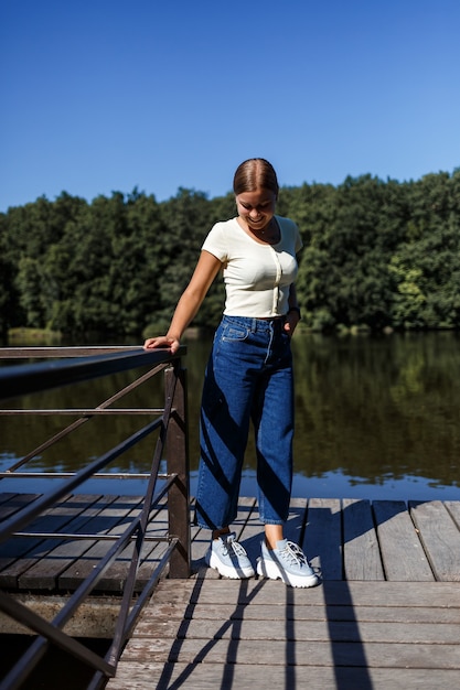 Una bella ragazza di aspetto europeo. Una giovane donna sta camminando lungo il fiume. Vestito con jeans e maglietta.