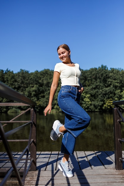 Una bella ragazza di aspetto europeo. Una giovane donna sta camminando lungo il fiume. Vestito con jeans e maglietta.