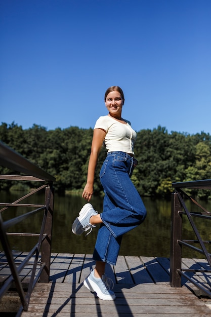 Una bella ragazza di aspetto europeo. Una giovane donna sta camminando lungo il fiume. Vestito con jeans e maglietta.