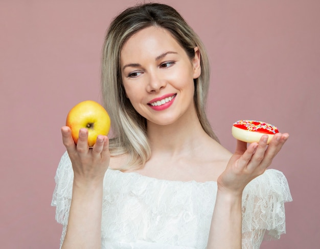 Una bella ragazza fa una scelta tra una mela e una ciambella