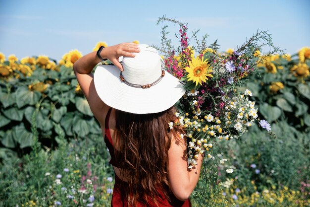 Una bella ragazza felice con un cappello di paglia è in piedi in un grande campo di girasoli